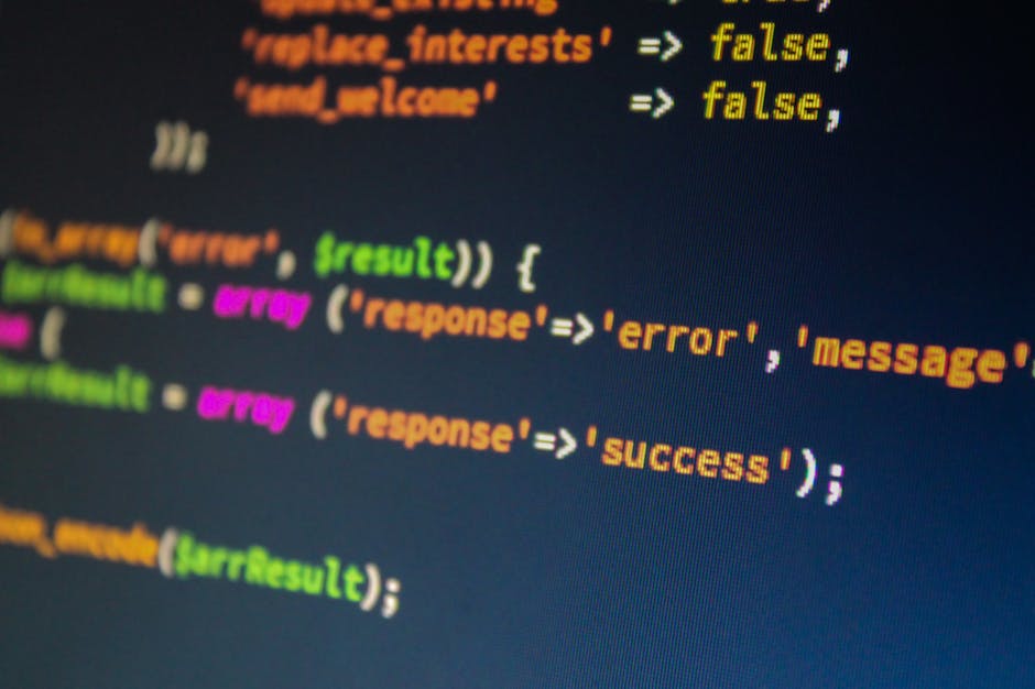 Close-up image of a computer screen displaying lines of colorful code in various shades of green, blue, orange, and purple on a dark background, with some areas showing blurred text and icons. The cod