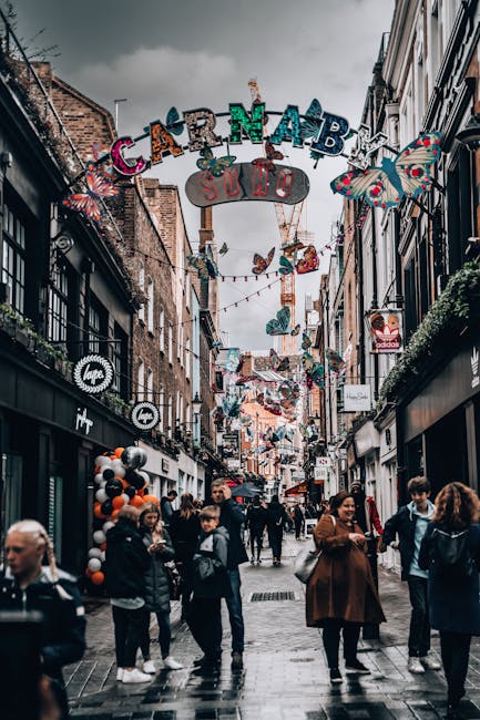 Decorative street lighting fixtures with gold-colored grid-like panels suspended above a narrow, bustling street on Carnaby Street, London, during daytime with overcast sky; surrounding architecture f